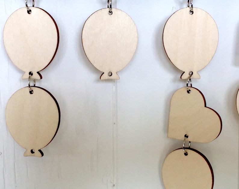 Puede incluir: Una guirnalda de madera con una cadena de adornos redondos y en forma de coraz&oacute;n. Los adornos est&aacute;n sin terminar y listos para ser pintados o decorados.