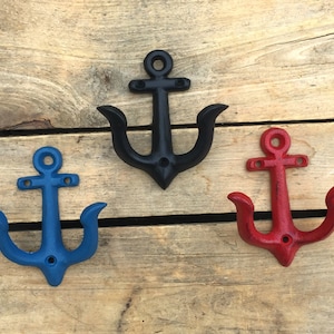 May include: Three cast iron anchor hooks in different colours: black, blue, and red. The hooks are mounted on a wooden surface.