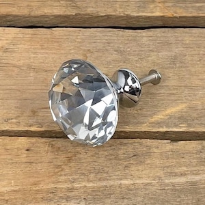 Peut inclure: Un bouton de meuble en cristal clair et facetté avec une base et une vis argentées polies. Le bouton est rond et a l'apparence d'un diamant. La quincaillerie est conçue pour les meubles et la décoration intérieure.