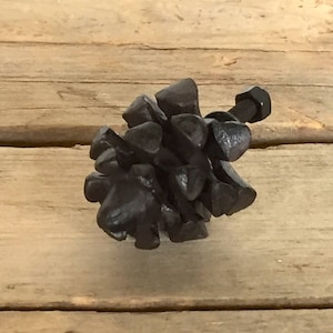 May include: A black cabinet knob with a distinctive, textured design. The knob is composed of small, irregular pieces clustered together, with a bolt extending from the back. The hardware is set against a wooden background.