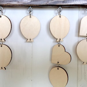 Puede incluir: Una guirnalda de madera con una mezcla de formas de coraz&oacute;n y globo, cada una con un agujero para colgar. La guirnalda est&aacute; hecha de madera sin terminar y est&aacute; lista para ser pintada o decorada.