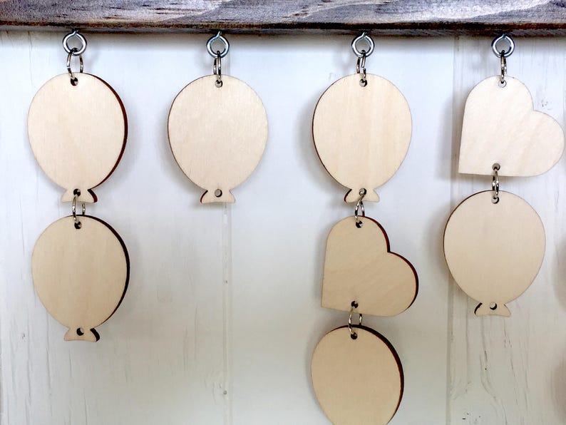 Puede incluir: Una guirnalda de madera con una mezcla de formas de coraz&oacute;n y globo, cada una con un agujero para colgar. La guirnalda est&aacute; hecha de madera sin terminar y est&aacute; lista para ser pintada o decorada.