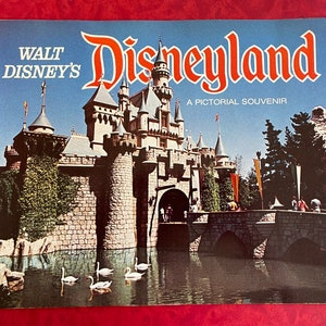 May include: A vintage book cover featuring a colorful illustration of Sleeping Beauty's castle at Disneyland. The text on the cover reads "Walt Disney's Disneyland A Pictorial Souvenir".