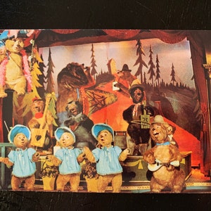 May include: A vintage postcard featuring a stage production of the classic children's story, "The Three Bears". The bears are dressed in colorful costumes and are performing on a stage with a backdrop of a forest. The postcard is in good condition and has a slight yellowing around the edges.