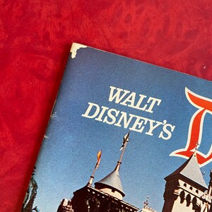 May include: A vintage Walt Disney's Disneyland guidebook with a blue cover and a picture of Sleeping Beauty's castle on the front.