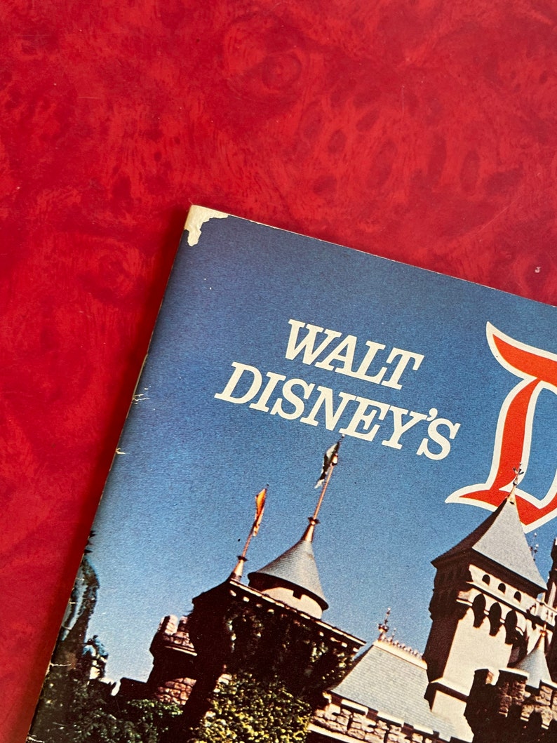 May include: A vintage Walt Disney's Disneyland guidebook with a blue cover and a picture of Sleeping Beauty's castle on the front.