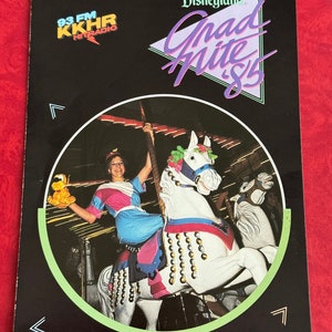 Puede incluir: Una fotografía en blanco y negro de una mujer montando un caballo de carrusel en Disneyland. La mujer lleva un vestido azul y rosa y sostiene un animal de peluche. La foto es de la década de 1980 e incluye el texto "Grad Nite '85" y "93 FM KKHR HITRADIO".