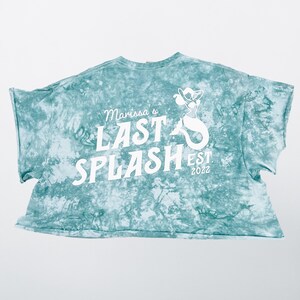 May include: A teal blue tie-dye cropped t-shirt with white text that reads "Marissa's Last Splash Est. 2022" and a white mermaid graphic.