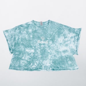 May include: A light blue tie-dye cropped t-shirt with a white seashell and the text "the bride" embroidered on the front.