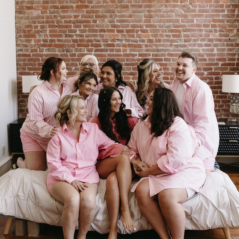 Puede incluir: Un grupo de personas con camisas de botones de color rosa claro a juego. Algunas camisas presentan un patr&oacute;n de rayas verticales blancas, mientras que otras son de color rosa claro s&oacute;lido. Tienen mangas largas, cuello y bolsillo.