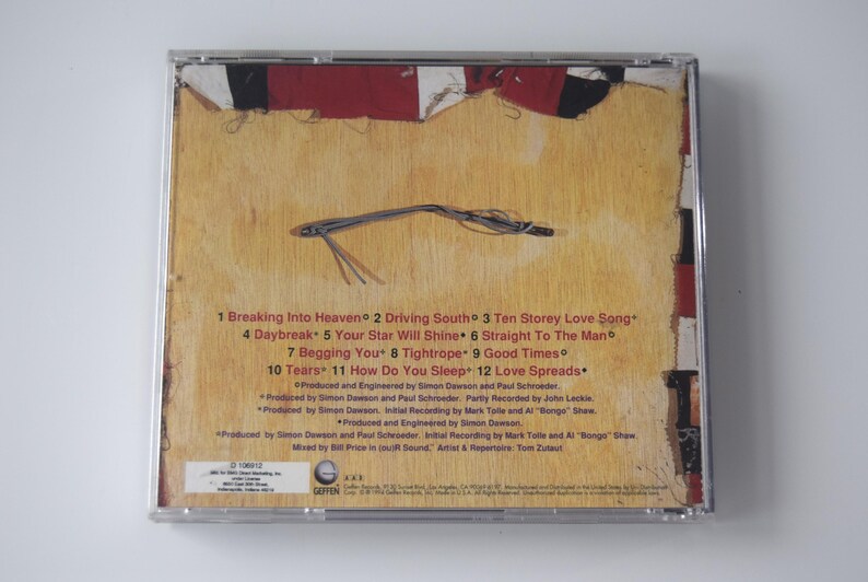 May include: A CD case with a textured, tan background and a design featuring red, white, and black elements. The back of the CD case displays a tracklist with song titles and production credits.