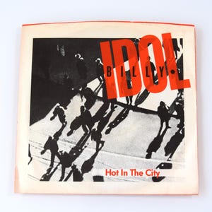 May include: A retro album cover with a monochrome image of people's silhouettes and shadows. The word "IDOL" is in large, bold, orange letters. The text "Hot In The City" is at the bottom of the cover.