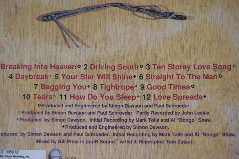 May include: A wooden surface with song titles and credits in red text. The titles include "Breaking Into Heaven," "Driving South," and "Ten Storey Love Song." A gray cord is at the top.