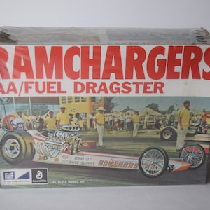 May include: A vintage model kit box for a 1/25 scale AA/Fuel Dragster. The box features a colorful illustration of the dragster, with the words "RAMCHARGERS" and "AA/FUEL DRAGSTER" in large red letters.