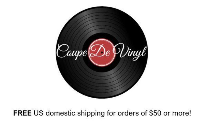 May include: A black vinyl record with the text "Coupe De Vinyl" in white script. The center label is red with a white border. The record is set against a white background.