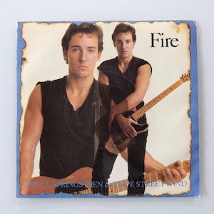 May include: A square vinyl record sleeve featuring a double exposure portrait of Bruce Springsteen wearing a black sleeveless shirt. He is holding an electric guitar. The text Fire is printed in the top right, and Bruce Springsteen & The E Street Band is at the bottom. The border has a blue, burnt-edge paper effect.
