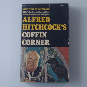 May include: A paperback book cover with a black background and yellow text. The title is "Alfred Hitchcock's Coffin Corner". The cover features a photo of Alfred Hitchcock and a raven.