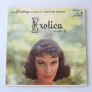 May include: Vintage vinyl record album cover for "Exotica Volume II" by Martin Denny. The cover features a woman with dark hair and dramatic eye makeup. The album title is in large, stylized letters.