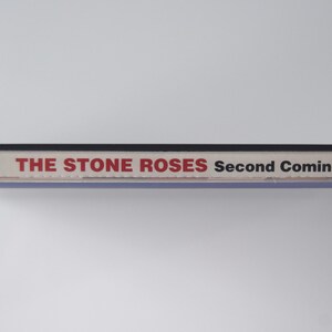 May include: A clear plastic CD case with the album title "Second Coming" by The Stone Roses. The text is in red and black. The case has the Geffen Records logo.