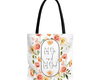 Puede incluir: Una bolsa de tela blanca con asas negras y un diseño floral. La bolsa tiene el texto "Let Go and Let God" en un óvalo negro.