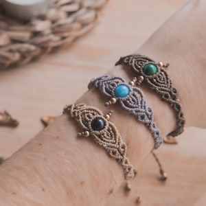 May include: Three macrame bracelets with different colored stones. The bracelets are made with a knotted cord and feature a small, round stone in the center of each bracelet. The stones are turquoise, green, and black.