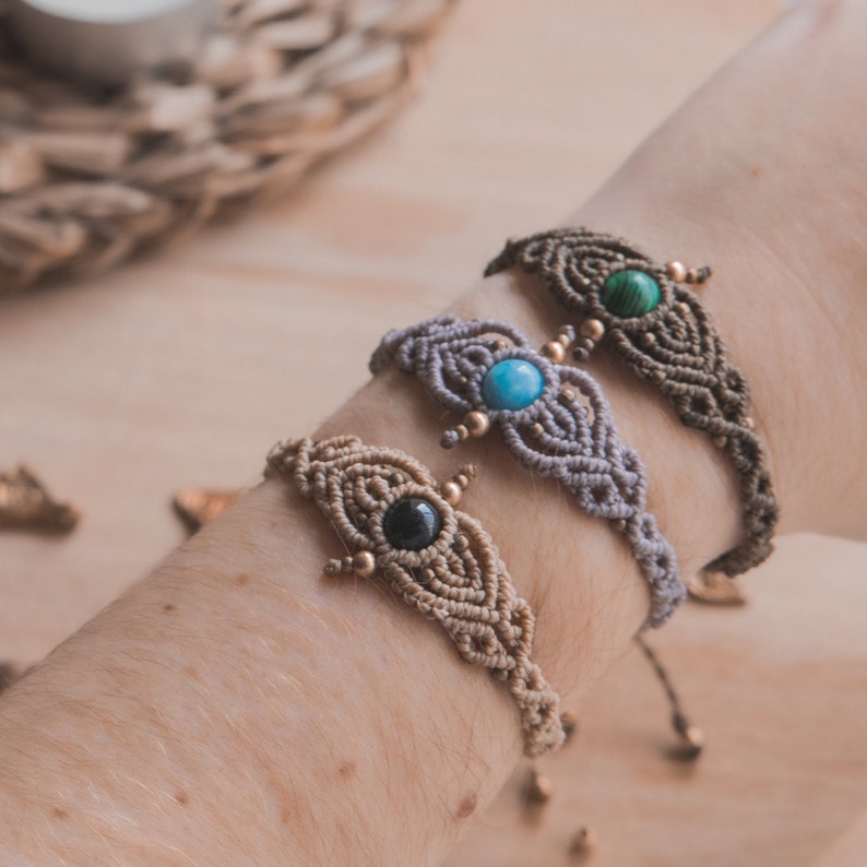 May include: Three macrame bracelets with different colored stones. The bracelets are made with a knotted cord and feature a small, round stone in the center of each bracelet. The stones are turquoise, green, and black.