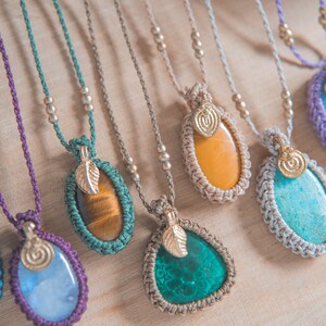 Puede incluir: Una colecci&oacute;n de collares de piedras preciosas hechos a mano. Cada collar presenta una piedra &uacute;nica de forma ovalada o de l&aacute;grima en varios colores, incluyendo azul, verde, amarillo y marr&oacute;n, engastada en un dise&ntilde;o de macram&eacute;. Los colgantes est&aacute;n adornados con dijes de hojas doradas y ensartados en collares de cord&oacute;n.