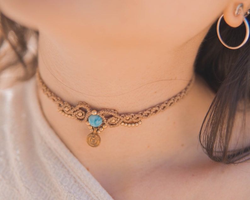 May include: A delicate brown macrame choker necklace with a blue gemstone pendant and a gold charm.