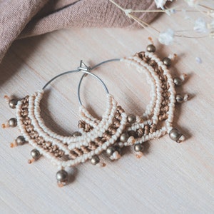 May include: A pair of hoop earrings with a macrame design in beige and brown with gold beads.