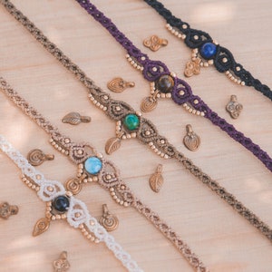 May include: Four macrame anklets with different colored cords and gemstone beads. The anklets are made with a variety of beads, including turquoise, lapis lazuli, tiger's eye, and onyx. Each anklet has a small brass charm hanging from it.
