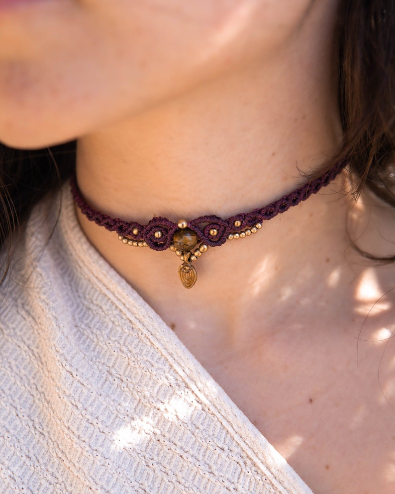 May include: A burgundy macrame choker necklace with a gold pendant and a tiger's eye stone.