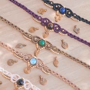May include: Four macrame anklets with different colored cords and gemstone accents. The anklets feature a variety of stones, including turquoise, lapis lazuli, tiger's eye, and onyx. Each anklet is adorned with small brass charms.