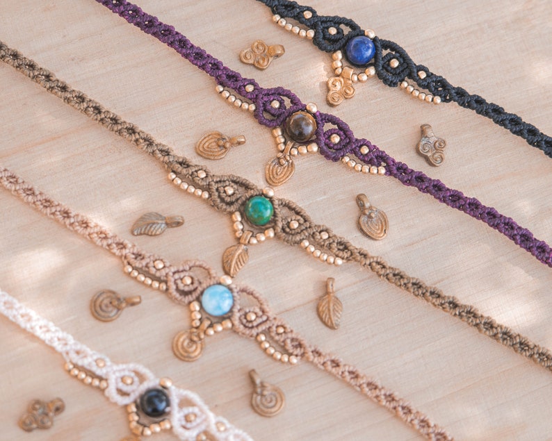 May include: Four macrame anklets with different colored cords and gemstone accents. The anklets feature a variety of stones, including turquoise, lapis lazuli, tiger's eye, and onyx. Each anklet is adorned with small brass charms.