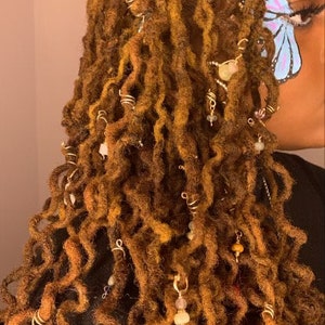 May include: Long brown dreadlocks with gold and silver beads and charms. The hair is styled with a butterfly design painted on the side of the face.