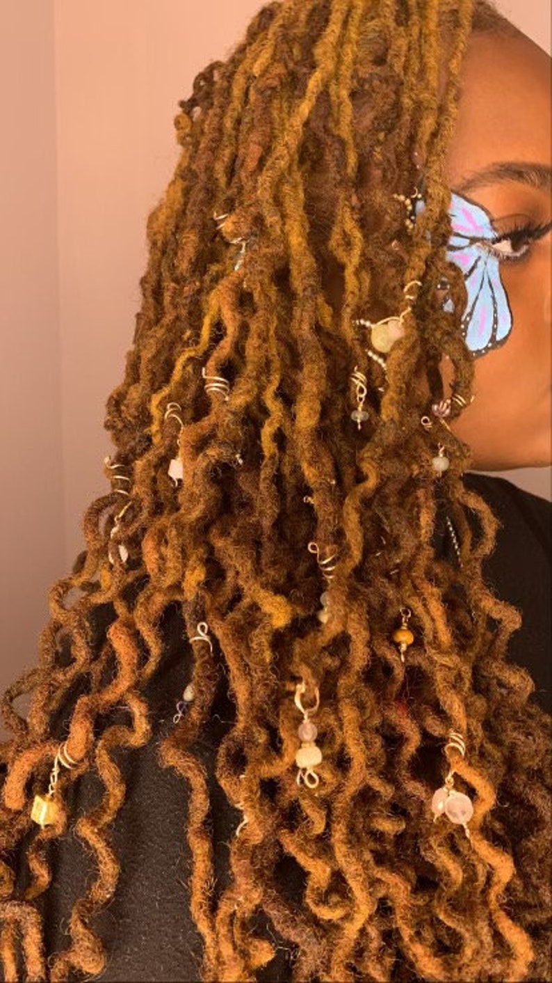 May include: Long brown dreadlocks with gold and silver beads and charms. The hair is styled with a butterfly design painted on the side of the face.