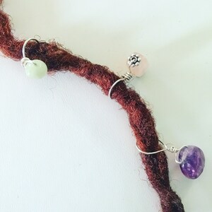 K&ouml;nnte beinhalten: Drei Perlen sind an einem braunen Dreadlock mit silbernem Draht befestigt. Die Perlen sind hellgr&uuml;n, hellrosa und violetter Amethyst.