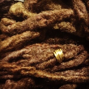 May include: Close-up of brown dreadlocks with a gold metal ring wrapped around one of the locks.