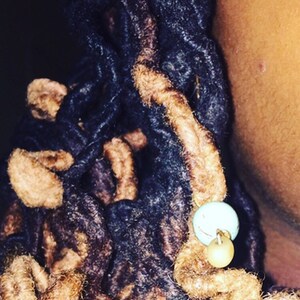 K&ouml;nnte beinhalten: Nahaufnahme von braunen und schwarzen Dreadlocks mit einem t&uuml;rkisfarbenen und beigefarbenen Perlenakzent.