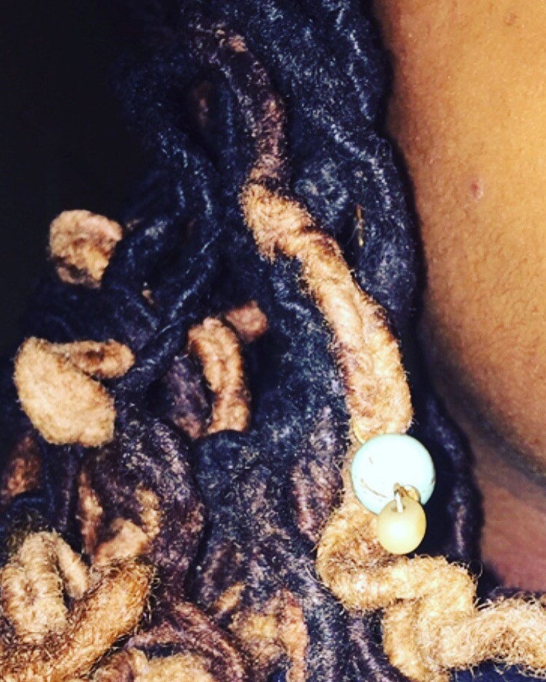 K&ouml;nnte beinhalten: Nahaufnahme von braunen und schwarzen Dreadlocks mit einem t&uuml;rkisfarbenen und beigefarbenen Perlenakzent.