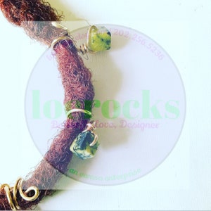 May include: Two gold-toned metal beads with green gemstone accents are attached to brown dreadlocks. The beads are wrapped with gold wire. The image includes the text "lo rocks" in a pink circle.