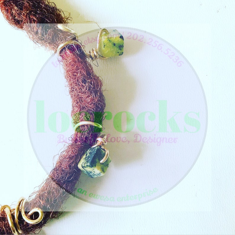 May include: Two gold-toned metal beads with green gemstone accents are attached to brown dreadlocks. The beads are wrapped with gold wire. The image includes the text "lo rocks" in a pink circle.