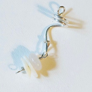 K&ouml;nnte beinhalten: Silberner Ohrring mit Spiraldesign und drei wei&szlig;en und rosafarbenen Steinen.