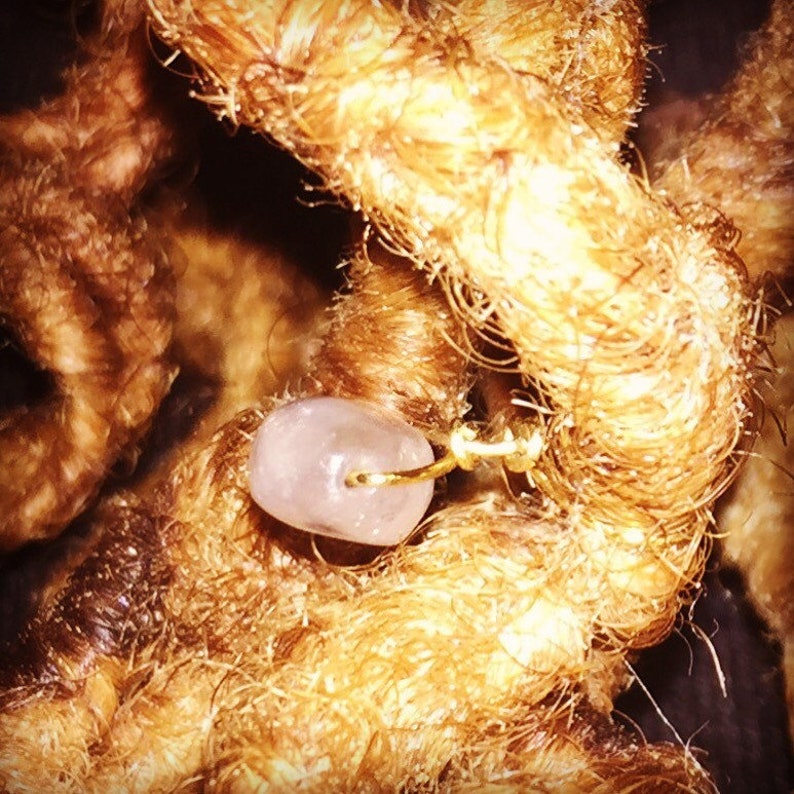 May include: A close-up of a light pink bead with a gold wire threaded through it. The bead is surrounded by brown hair.