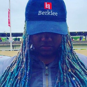 K&ouml;nnte beinhalten: Eine Person mit langen blauen und gr&uuml;nen Dreadlocks tr&auml;gt eine dunkelblaue Baseballkappe mit einem wei&szlig;en Logo, auf dem "Berklee" steht, und einem roten Quadrat mit dem Buchstaben "B" darin.