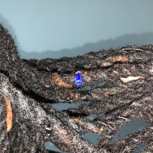 K&ouml;nnte beinhalten: Nahaufnahme von Dreadlocks einer Person mit einem kleinen blauen Edelstein-Ohrring.