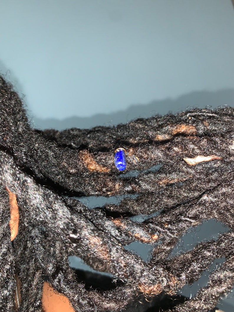 K&ouml;nnte beinhalten: Nahaufnahme von Dreadlocks einer Person mit einem kleinen blauen Edelstein-Ohrring.