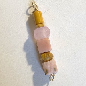 May include: A gold charm with a series of pink and brown gemstone beads. The beads are strung on a gold wire and the charm has a gold loop at the top.