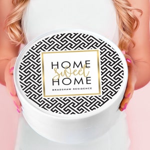 May include: White round box with a black and white geometric pattern and gold lettering that says "Home Sweet Home Bradshaw Residence".