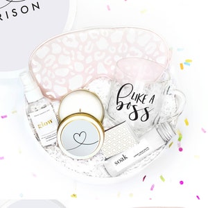 Puede incluir: Una caja de regalo blanca llena de art&iacute;culos de cuidado personal, que incluyen una taza que dice "Like a Boss", una vela, sales de ba&ntilde;o y una m&aacute;scara para dormir. La caja est&aacute; decorada con un coraz&oacute;n y el nombre "Harrison".