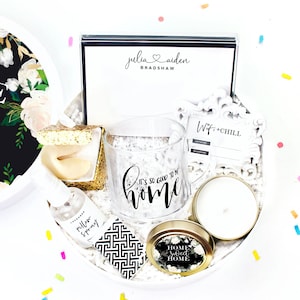 May include: A white gift box filled with housewarming gifts, including a glass mug that says "It's so good to be home", a candle, a pillow spray, and a box of matches. The box is decorated with confetti and the text "White Confetti Box".